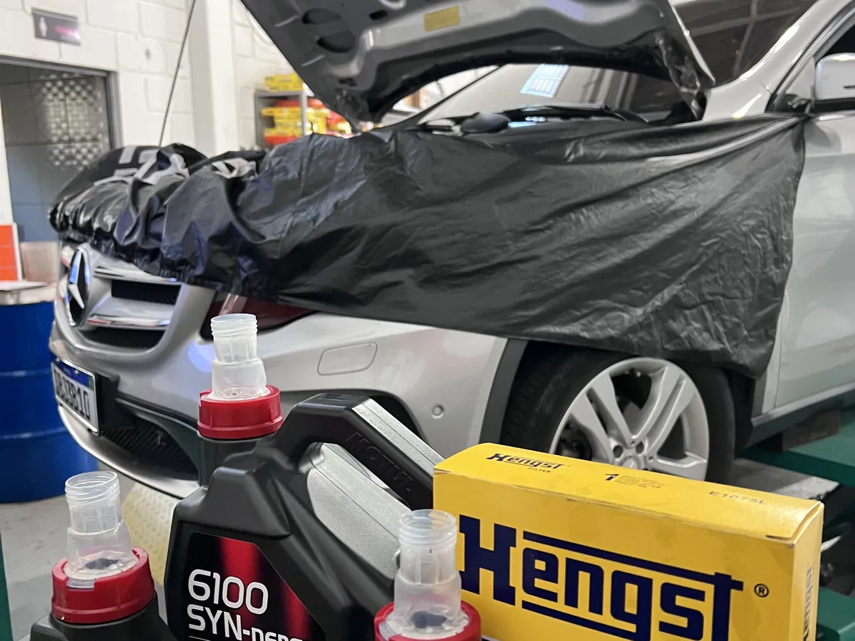Mercedes com capô aberto na oficina, com frascos de óleo e filtro Hengst na frente