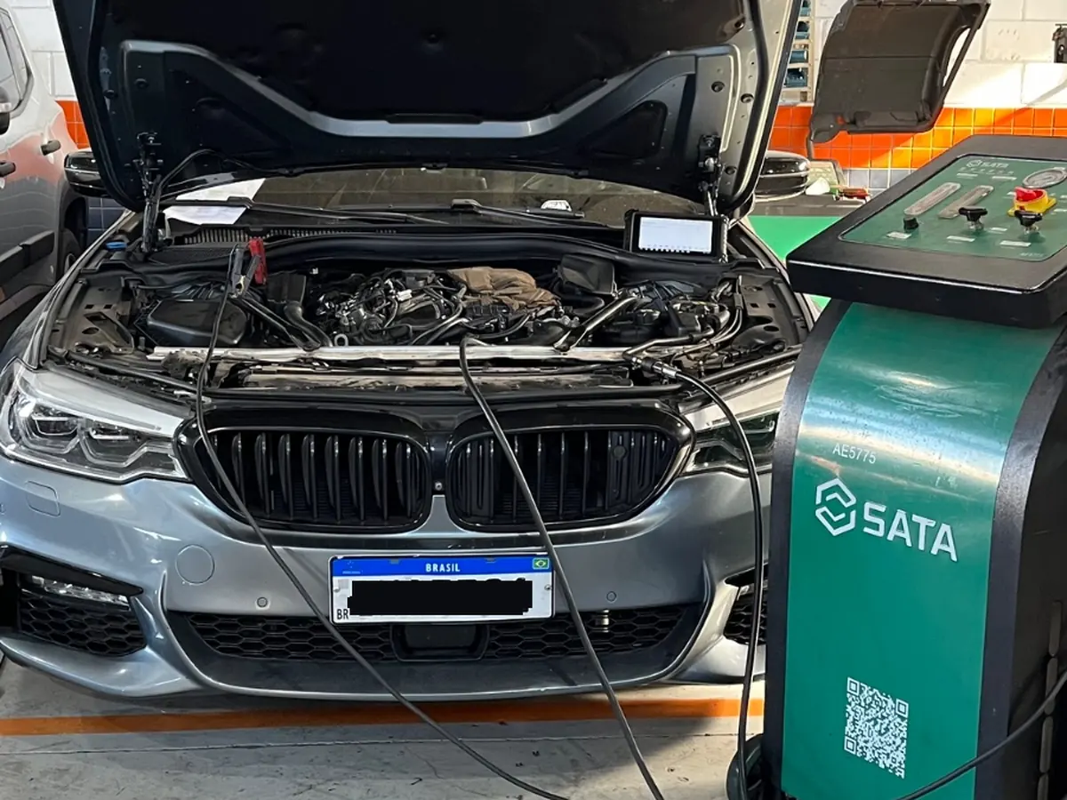 BMW com capô aberto na oficina, com máquina de troca de fluido SATA ao lado